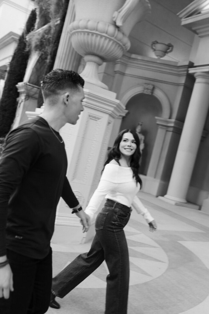 Black and white photo o a couple holding hands and walking outside of Caesars Palace for their Las Vegas engagement photos.