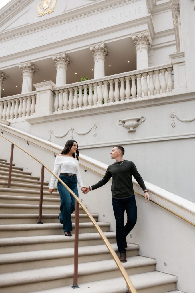 Couple holding hands and walking down a staircase for their Las Vegas engagement photos at Caesar's Palace. 