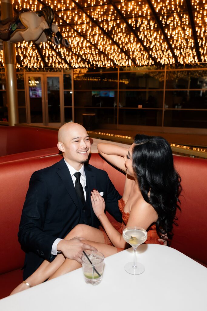 Couple sitting in a booth and having drinks during their Fremont Street engagement photos in Las Vegas.