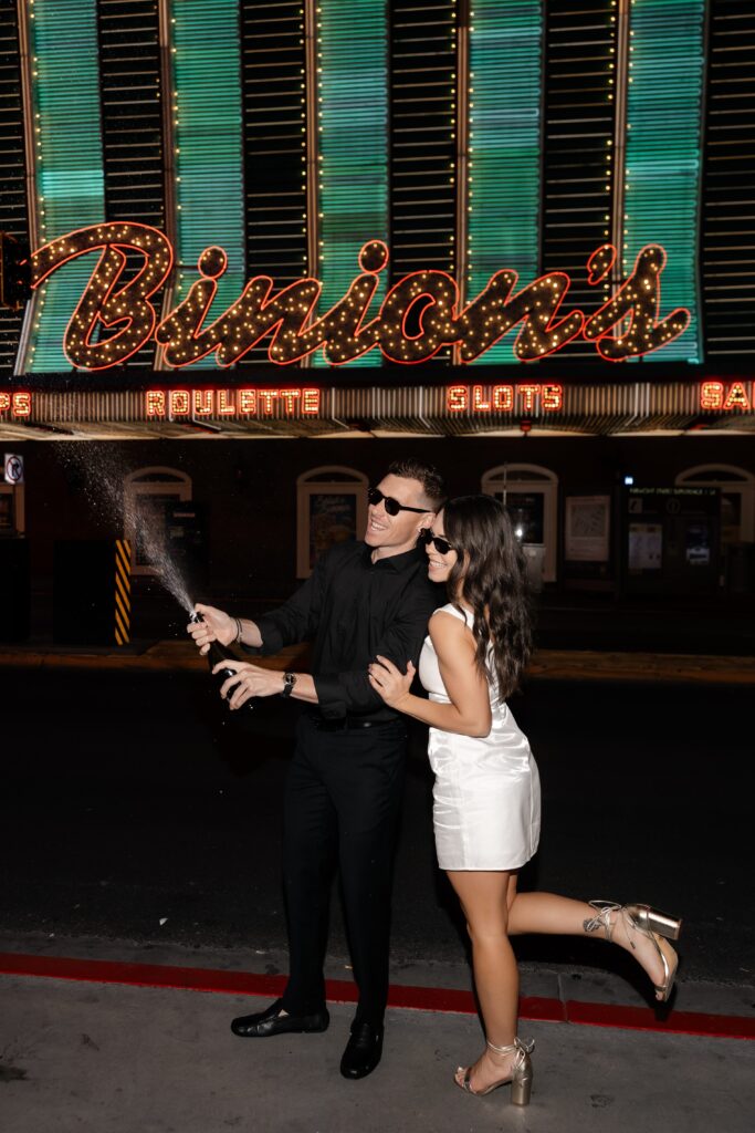 Couple popping champagne in front of Binion's for their Las Vegas engagement photos.