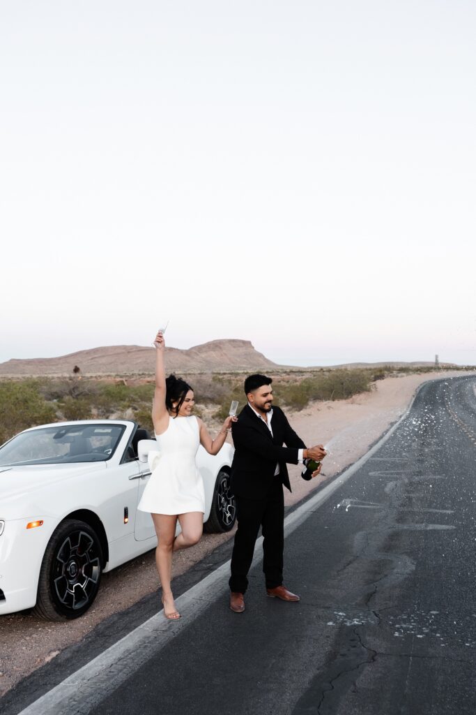 Couple popping champagne during their Las Vegas engagement photos in the desert. 