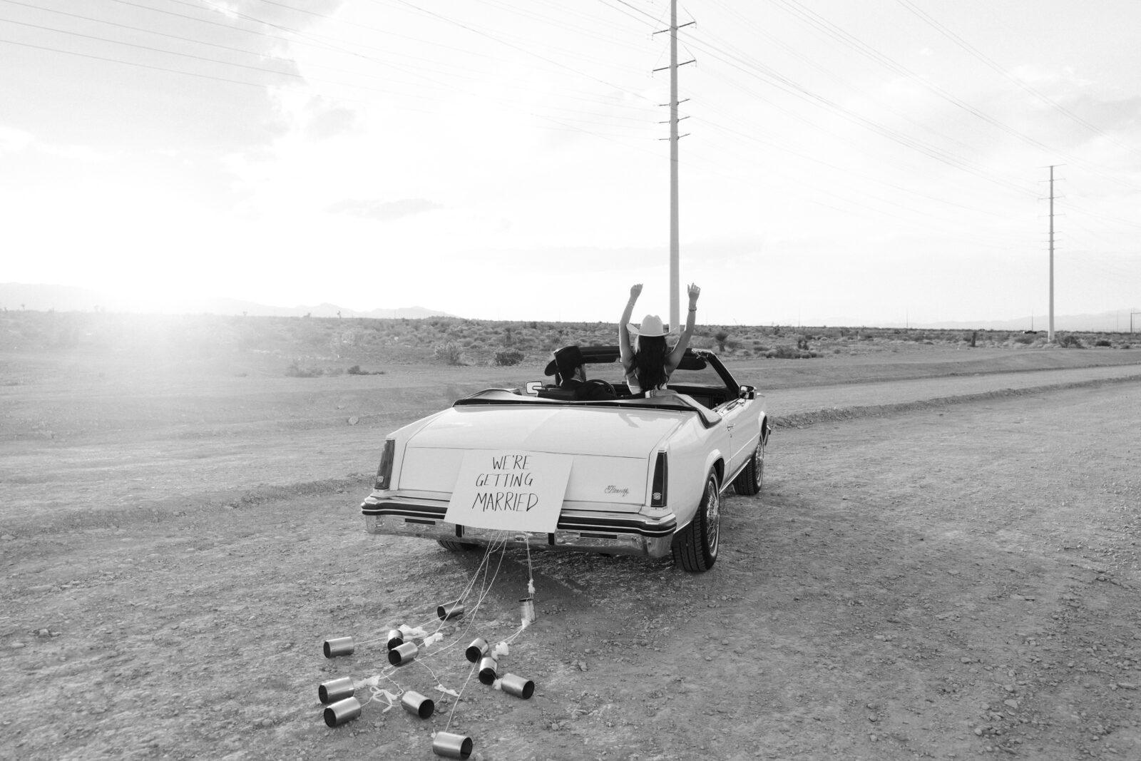 Black and white wide shot of a couple riding off in a car for their wedding announcement photos in the Las Vegas desert. 