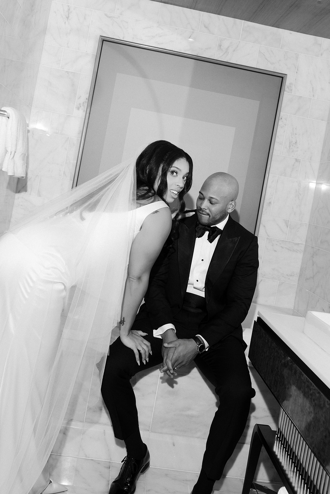 Black and white photo of a bride and groom posing in the bathroom of their hotel suite. 
