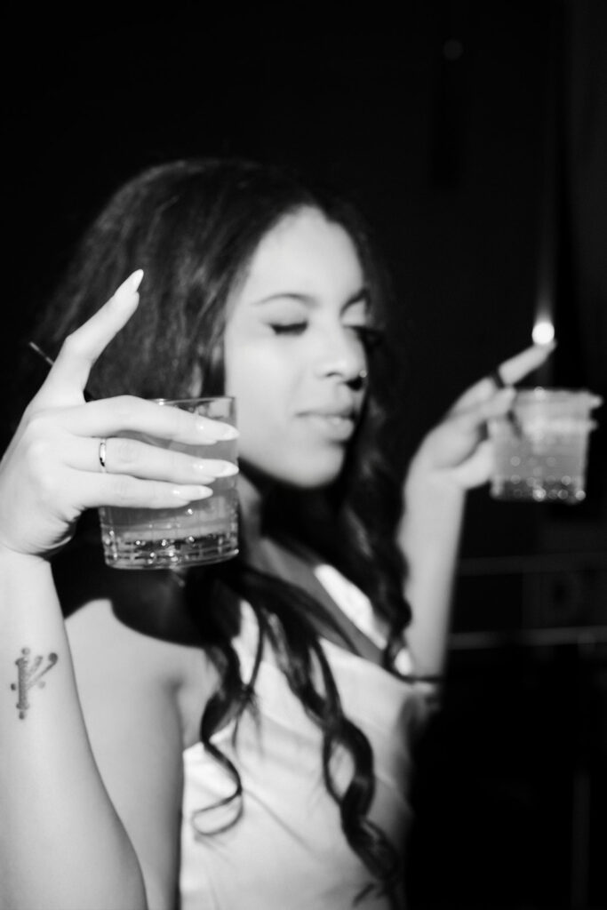 Black and white photo of the bride holding two drinks in her hand.