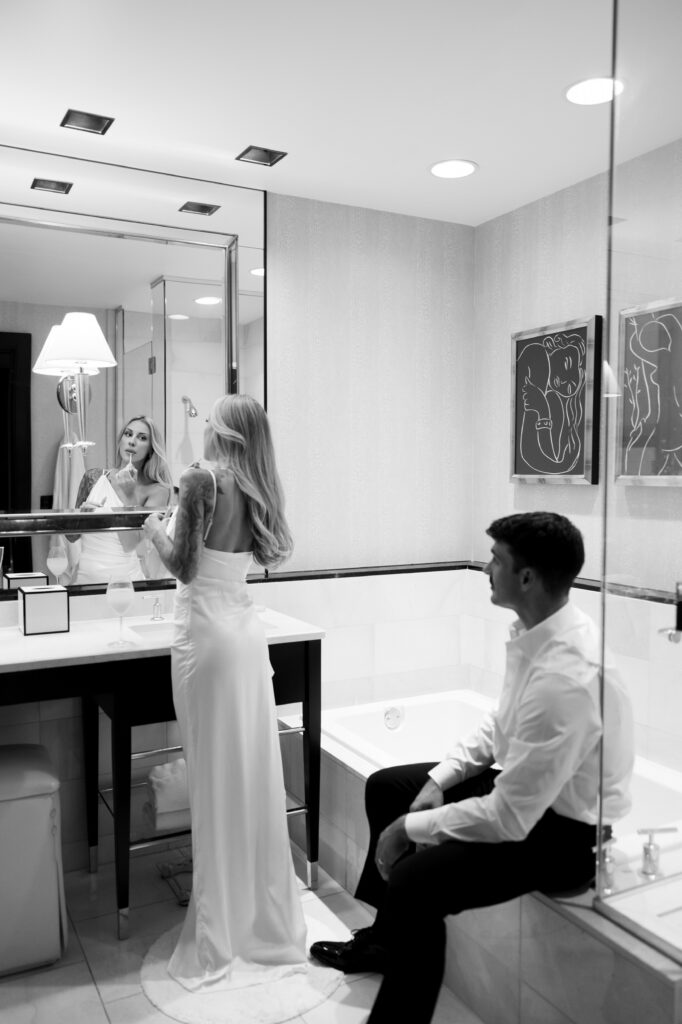 Black and white photo of a bride and groom getting ready in their bathroom hotel suite together. 