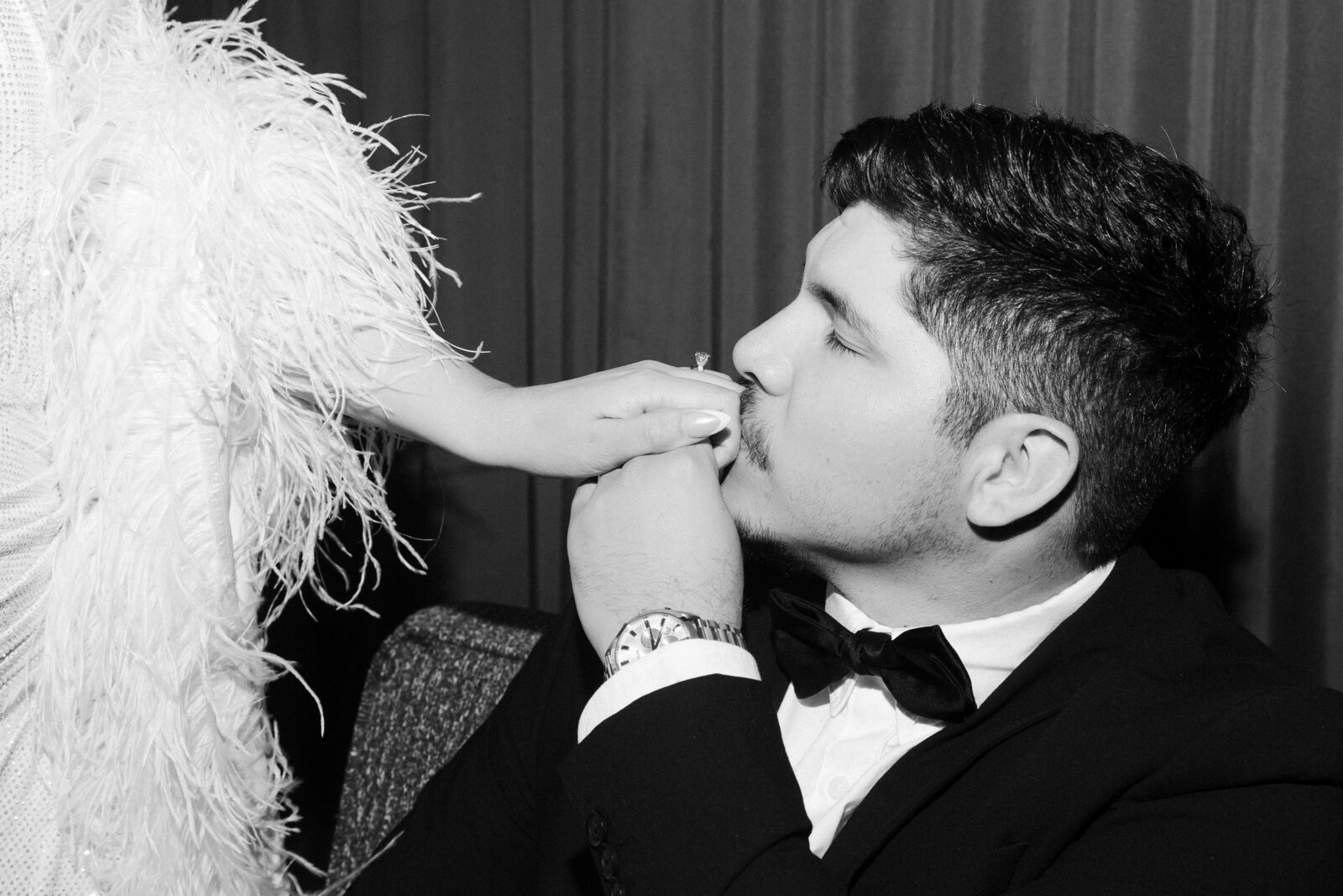 Black and white portrait of a groom kissing his brides hand.