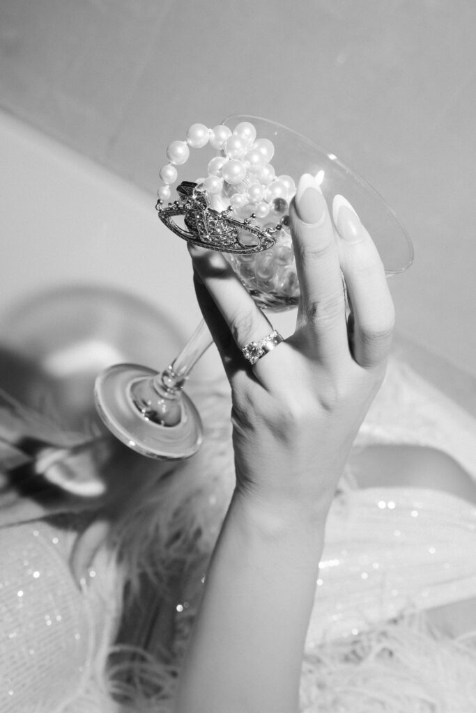 Black and white photo of a bride holding a glass with jewelry in it. 