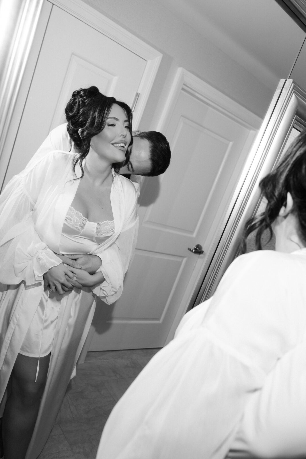 Black and white photo of a bride and groom getting ready together in their hotel room.