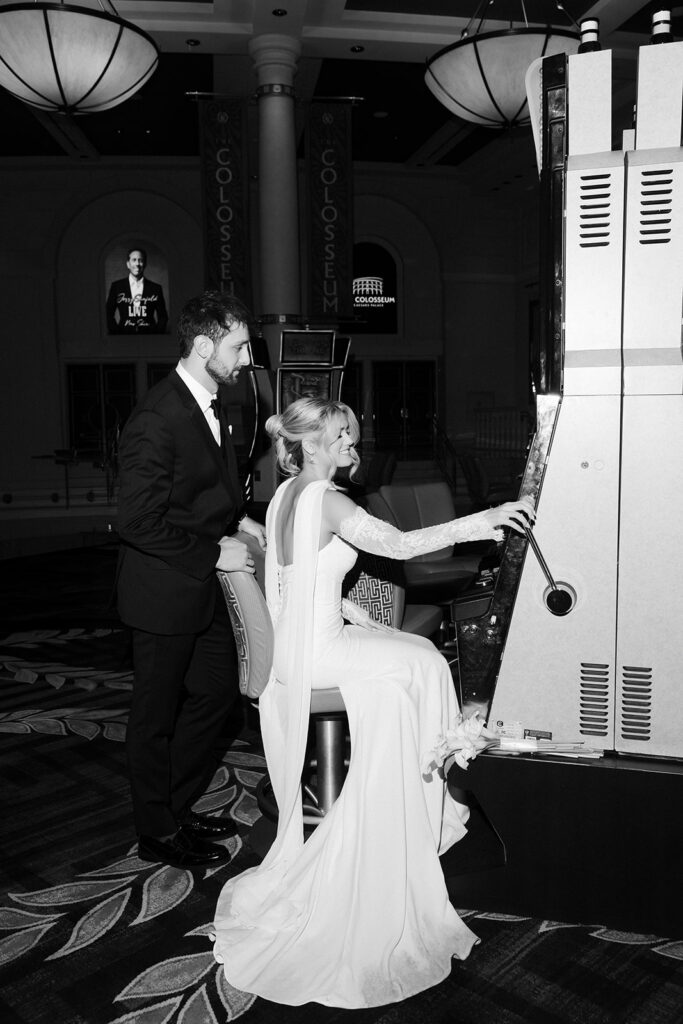 Black and white photo of a bride and groom playing the slot machines inside the Caesars Palace casino in Las Vegas. 