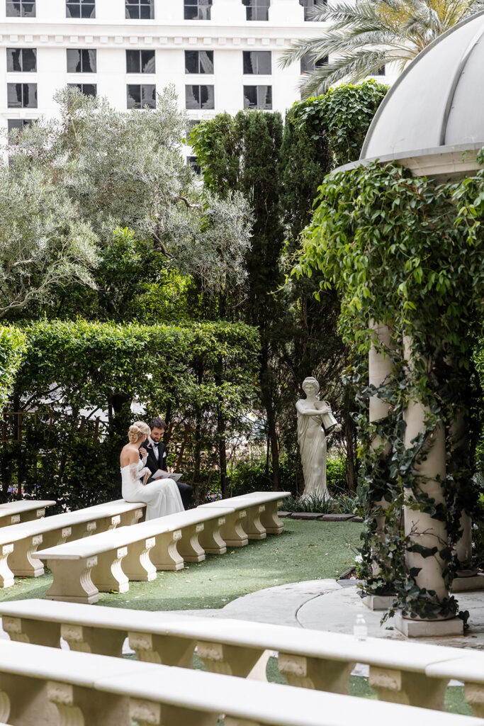 Newlywed bride and groom sitting together on garden benches at Caesars Palace after their ceremony.