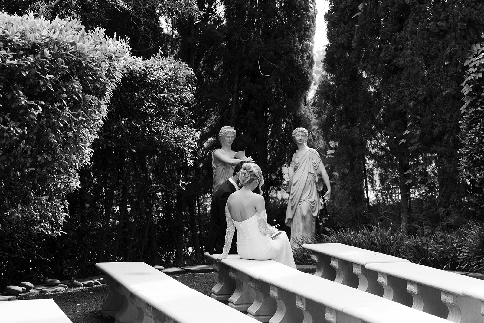 Newlywed bride and groom sitting together on garden benches at Caesars Palace after their ceremony.