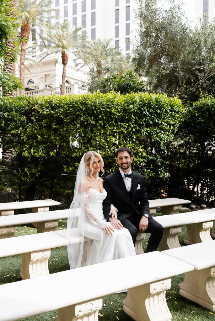 Newlywed bride and groom sitting together on garden benches at Caesars Palace after their ceremony.