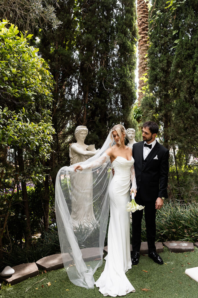 Bride and groom standing beside statues in the garden near the Venus Garden Chapel at Caesars Palace.