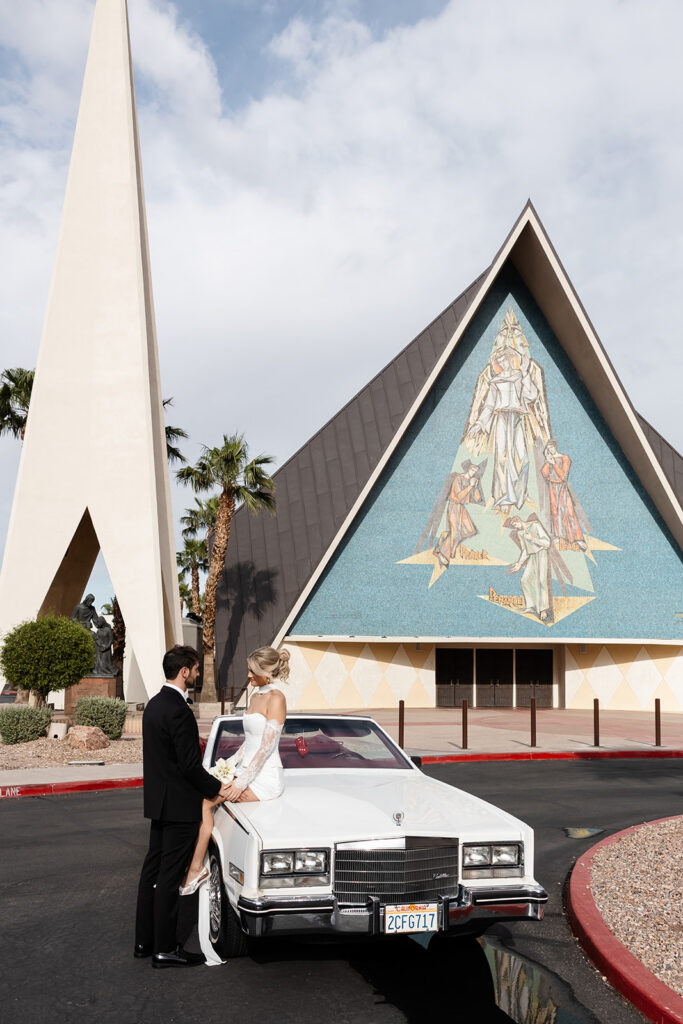 Bride and groom posing with a classic convertible outside of Guardian Angel Cathedral in Las Vegas.