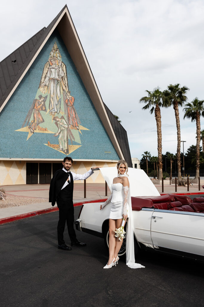 Bride and groom posing with their vintage convertible outside Guardian Angel Cathedral in Las Vegas.