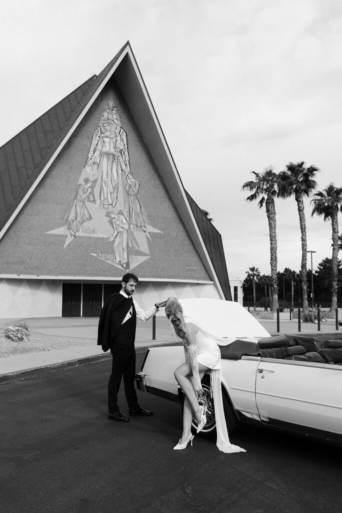 Black and white editorial wedding photo of a bride and groom posing with Risky Ride outside Guardian Angel Cathedral in Las Vegas.