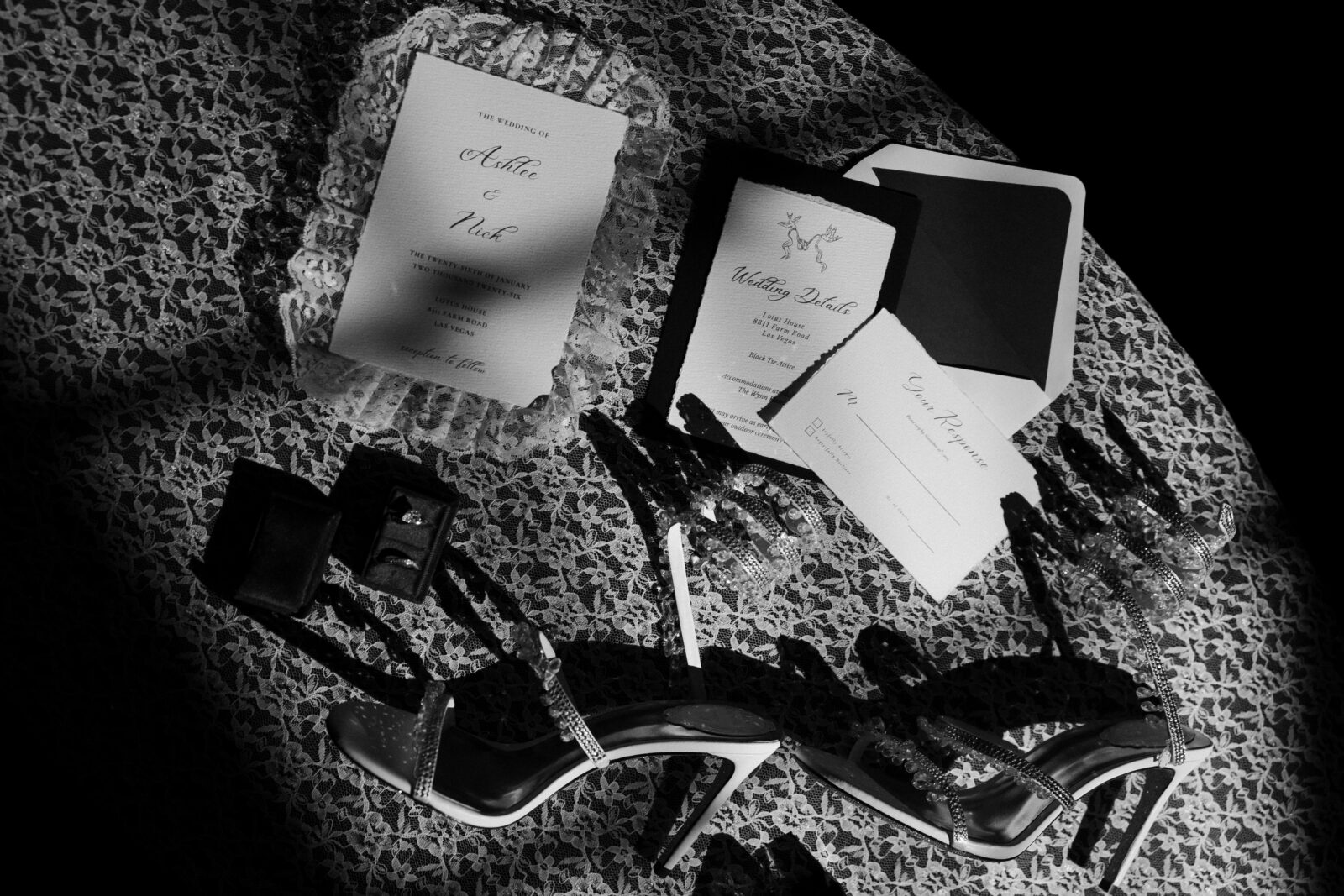 Black and white photo of luxury wedding details with stationary, jewelry, heels.