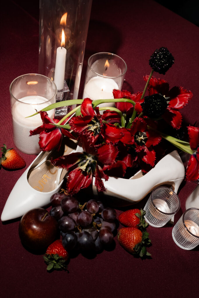 Editorial flash wedding detail shot with fruit, florals, candles, and white heels.