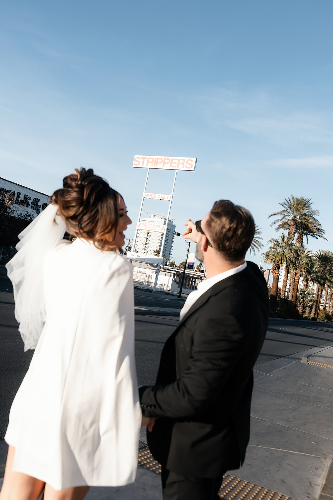 Bride and groom laughing and pointing to the strippers sign in Las Vegas,