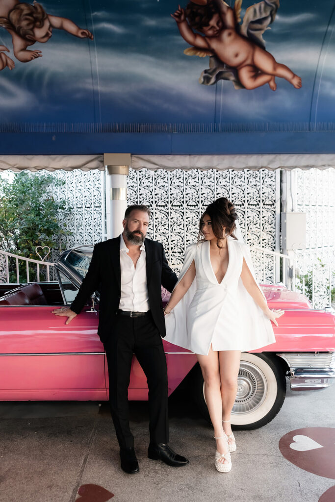Bride and groom leaning against the pink Cadillac at The Little White Wedding Chapel.