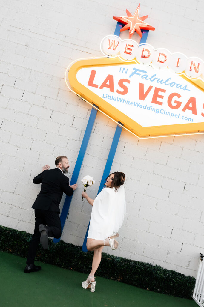 Bride and groom posing under a Las Vegas sign outside of The Little White Wedding Chapel in Las Vegas.