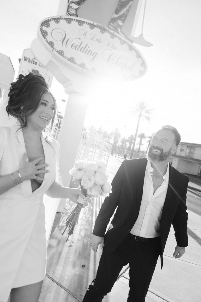 Bride and groom laughing together outside The Little White Wedding Chapel sign in Las Vegas.