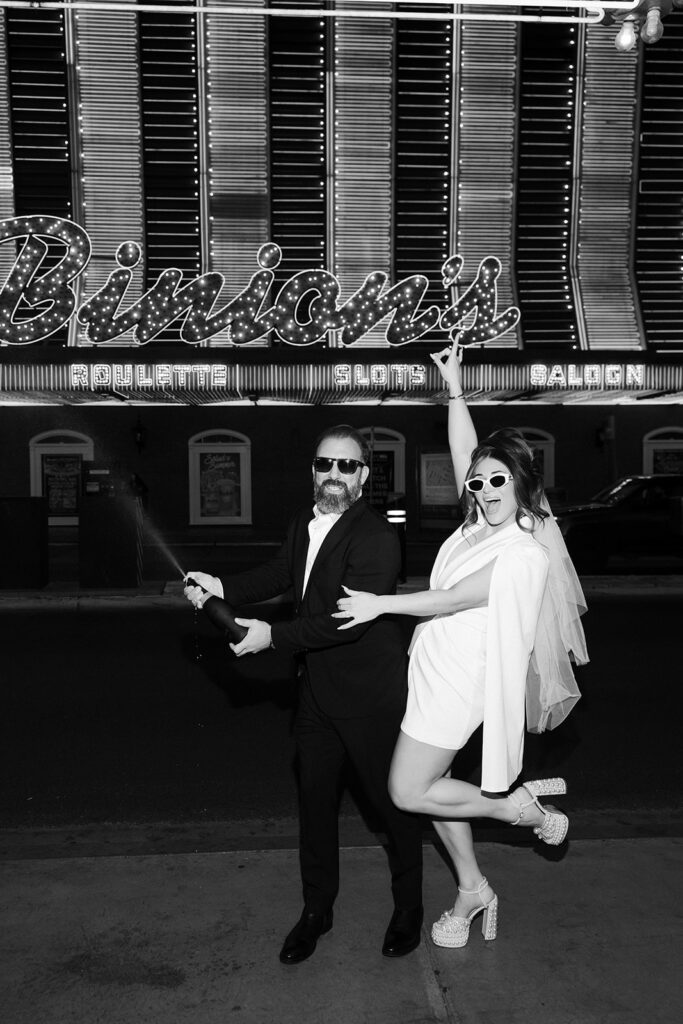 Bride and groom celebrating with champagne in front of the Binion’s casino sign on Fremont Street in Las Vegas.
