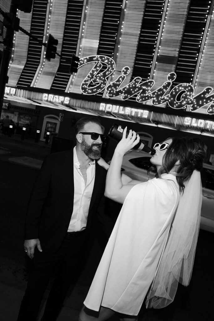 Bride and groom celebrating with champagne in front of the Binion’s casino sign on Fremont Street in Las Vegas.
