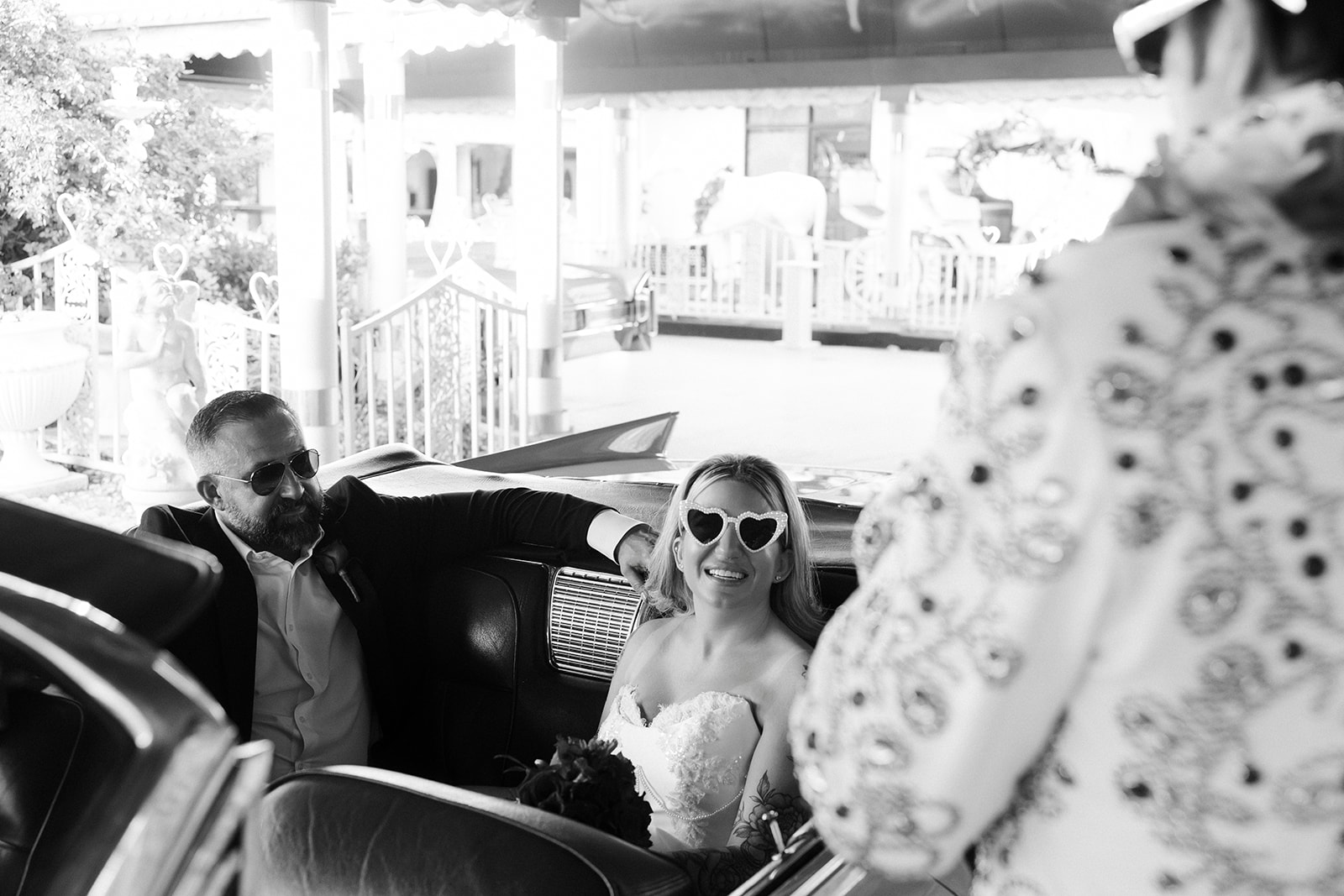 Black and white photo of a bride and groom sitting in the back of the pink Cadillac for their Las Vegas vow renewal with Elvis. 