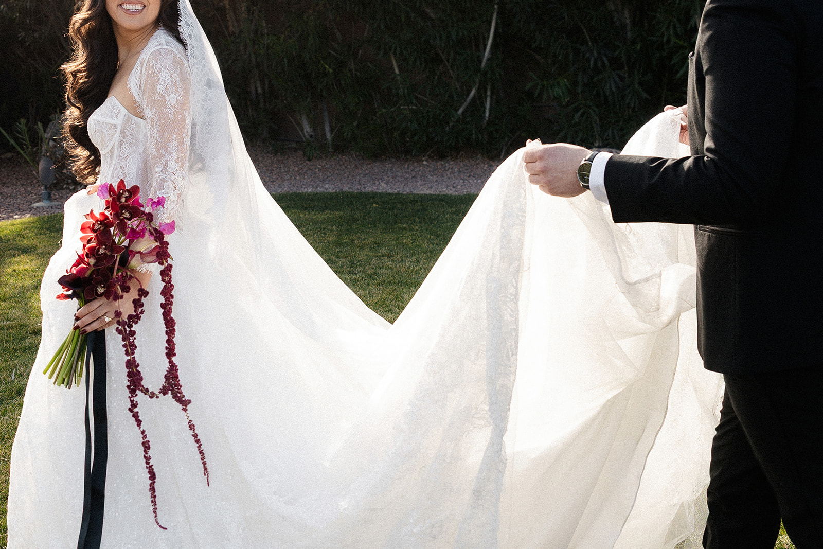 Close up shot of a bride walking with the groom trailing behind her and holding up her train.