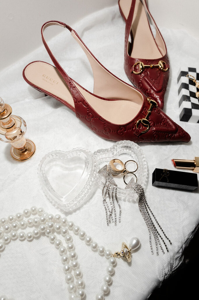 Luxury wedding details with rings, jewelry, lipstick, and red heels.