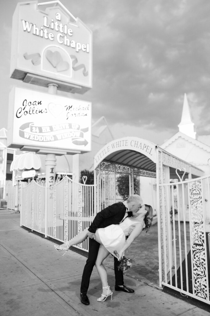 Black and white photo of a bride and groom kissing in front of The Little White Wedding Chapel.