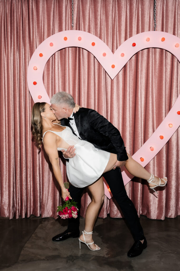 Bride and groom kissing in front of the pink heart at Sure Thing Chapel for their Las Vegas vow renewal. 