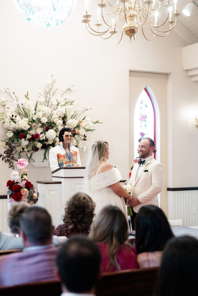 Bride and groom holding hands at the altar while the Elvis impersonator gives a speech during the ceremony.