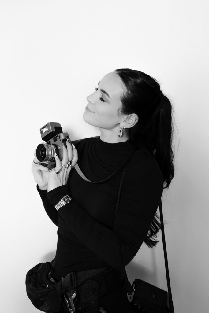 Black and white photo of Kyra, Las Vegas wedding and elopement photographer and owner of Risky Exposure Photography posing with her camera.