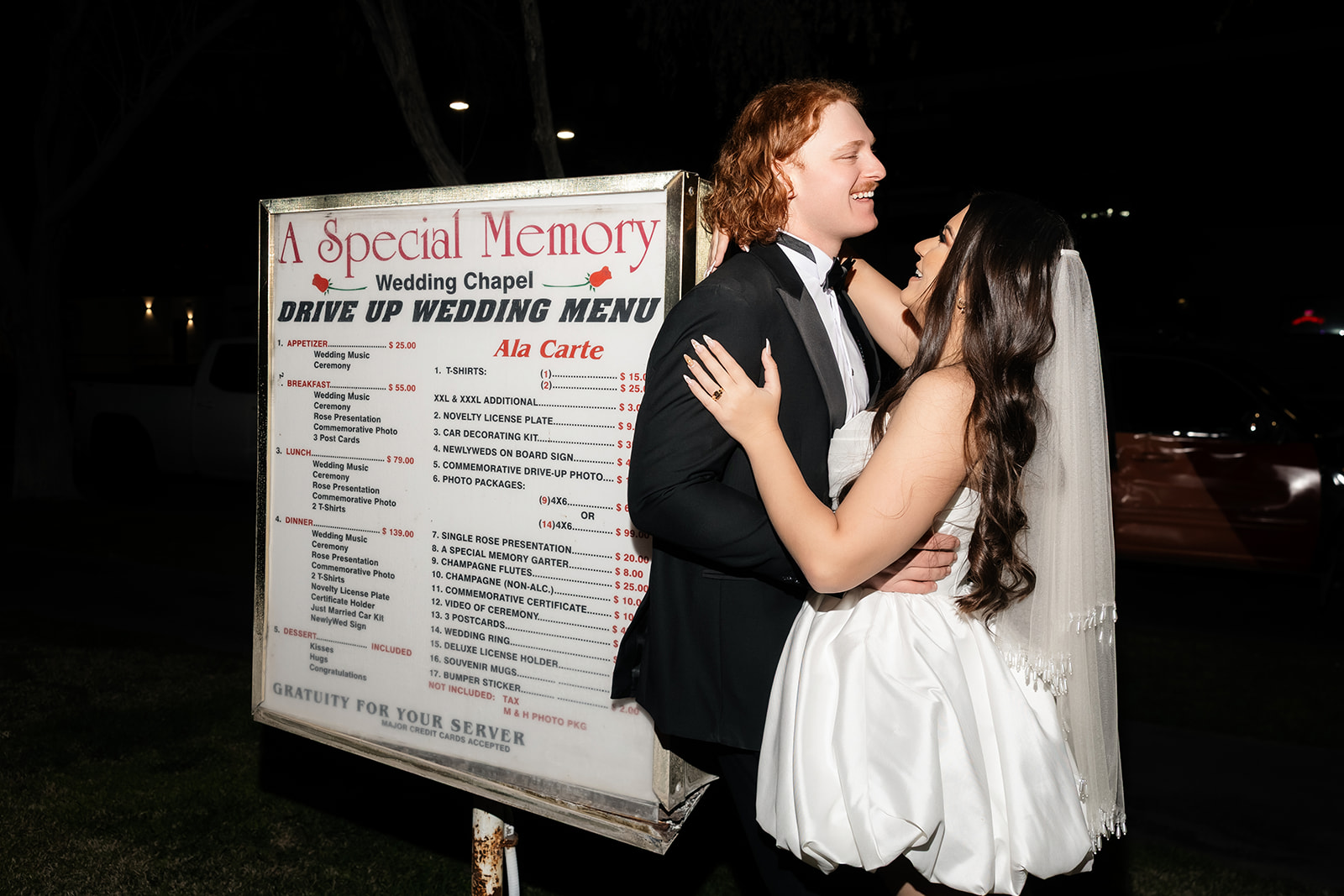 Couple posing next to A Special Memory Wedding Chapel's drive-up wedding menu sign.