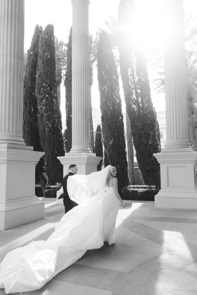Black and white photo of a bride and groom walking through Caesars Palace. 