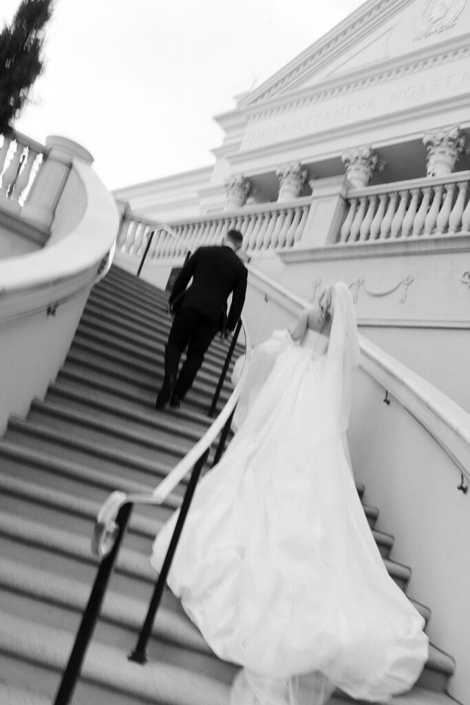 Black and white photo of a bride and groom walking up the stairs.