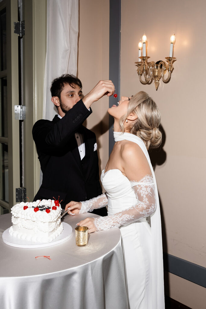 Groom feeding the bride a cherry off of their cake during their Las Vegas wedding reception at Canaletto at The Venetian.