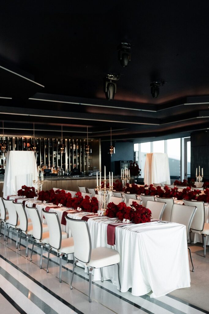 Deep red rose wedding centerpieces with candlelight and gold table numbers at a Ghostbar reception.