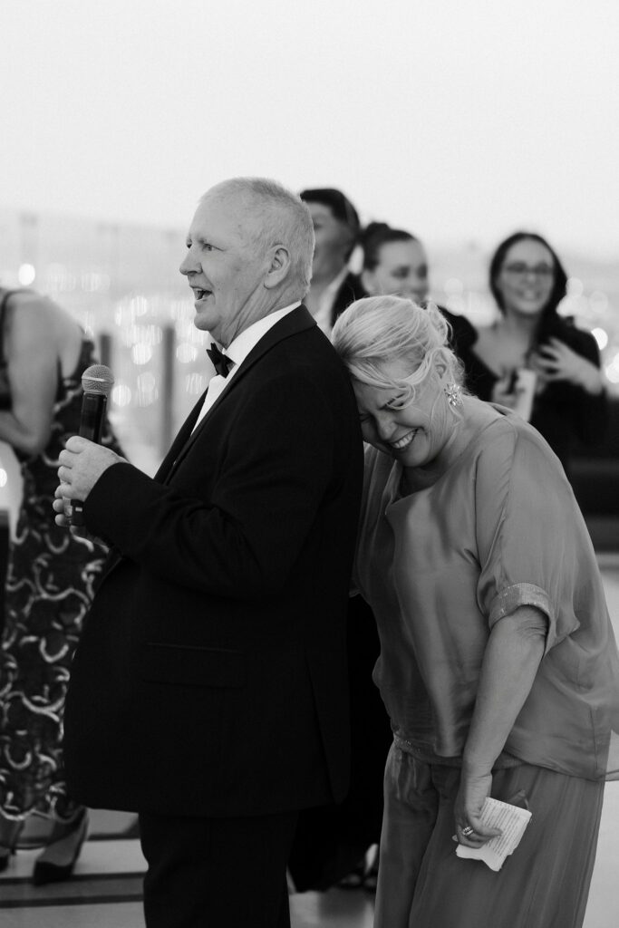 Mother of the groom laughing as the grooms father gives a speech during a Las Vegas rooftop wedding reception at Ghostbar at The Palms.