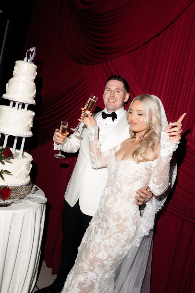 Bride and groom posing playfully next to their cake and with glasses of champagne. 