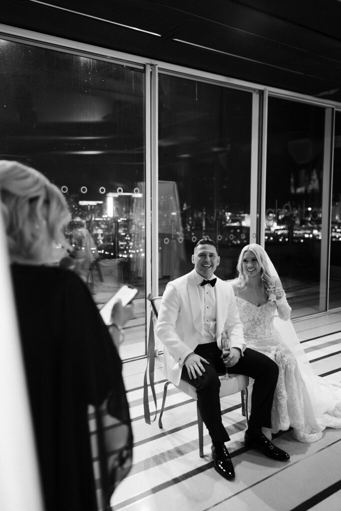 Black and white photo of a bride and groom sitting together during speeches.