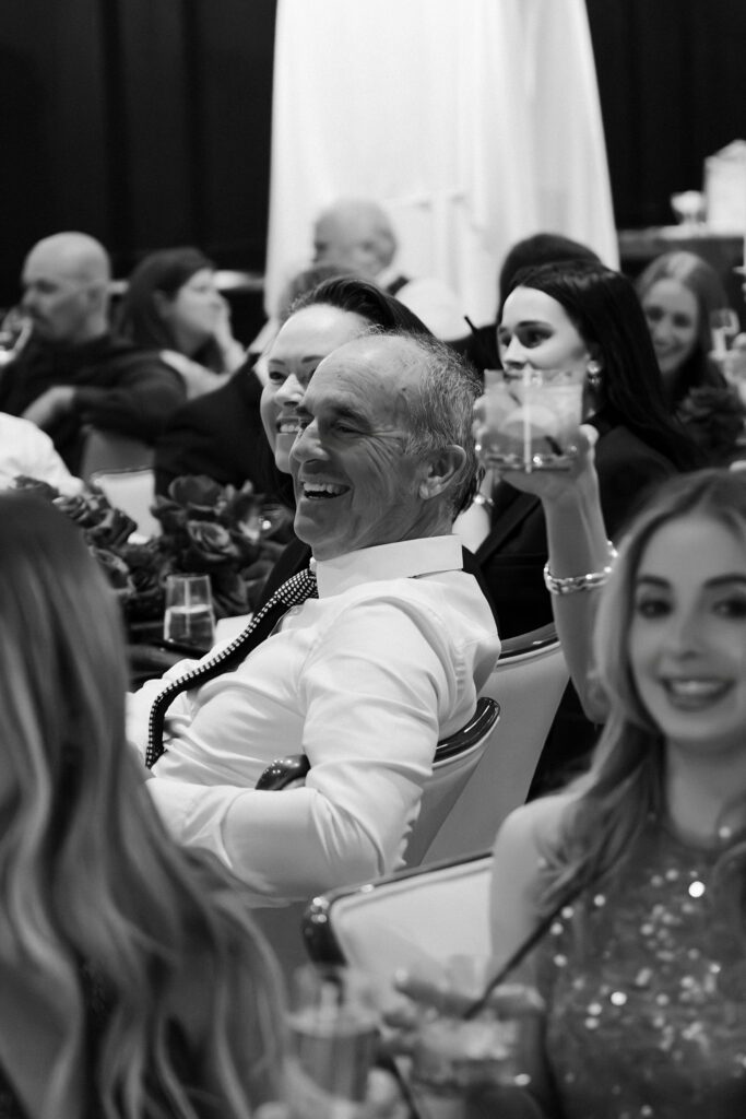 Black and white photo of guests listening and raising glasses during a Las Vegas wedding reception.