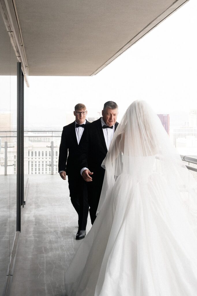 Bride walking toward her father and brother on a balcony before her Las Vegas wedding ceremony for a first look.