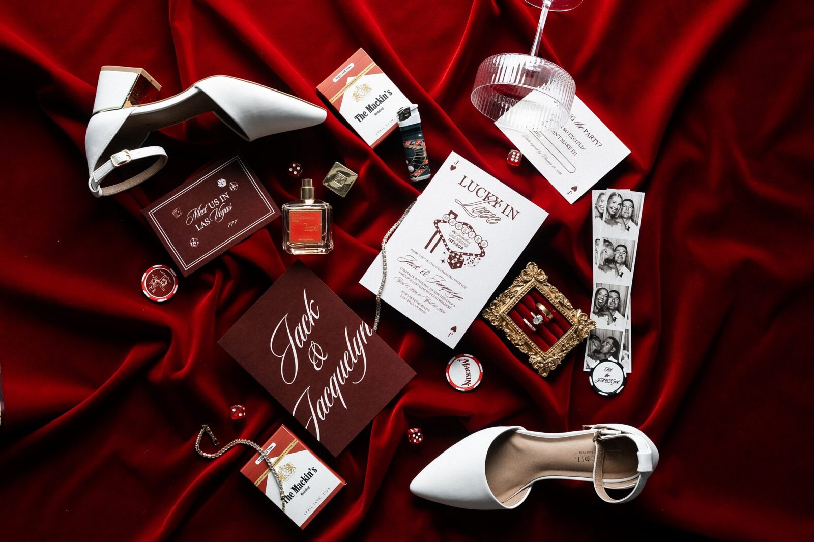 Las Vegas wedding details with white shoes, invitation suite, matchbooks, playing cards, and ring on red fabric.