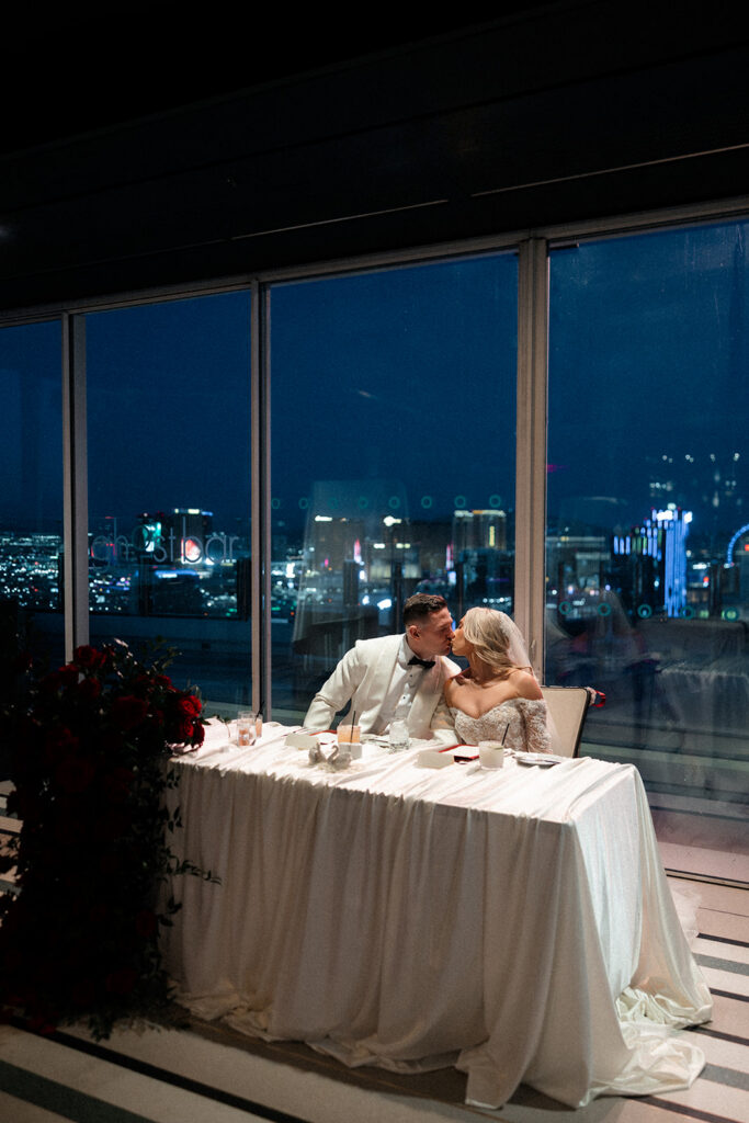 Bride and groom kissing at their sweethearts table during their Ghost Bar Las Vegas wedding reception at The Palms.