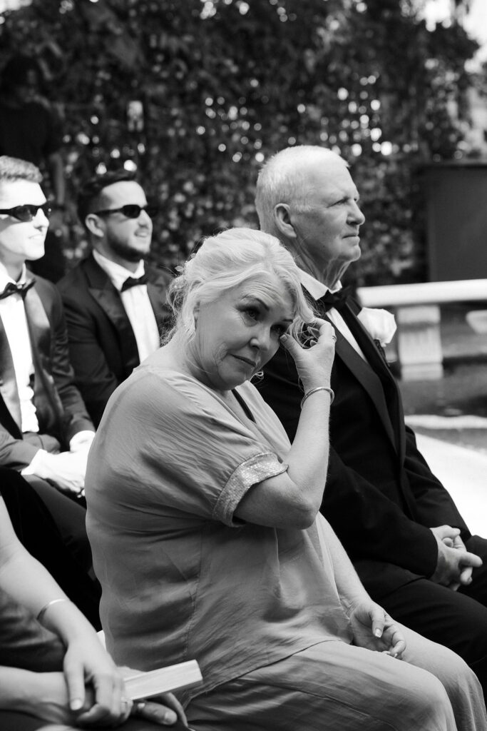 Black and white photo of the grooms mother wiping tears away during the ceremony.