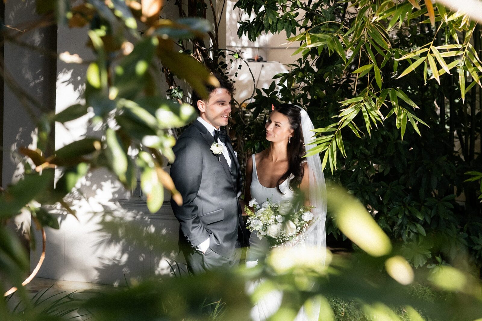 Bride and groom posing surrounded by greenery.