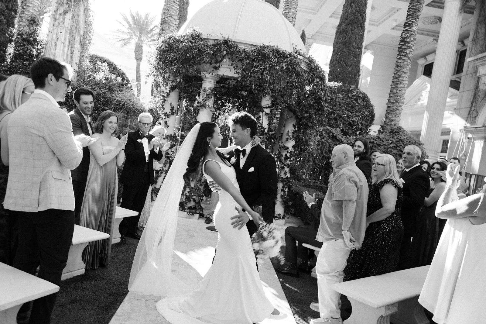 Black and white photo of a bride and grooms dip kiss at the end of the aisle at Venus Garden Caesars Palace.